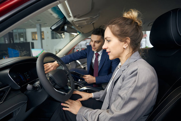 Empresario mostrando a una mujer en una chaqueta el panel de control de un coche - Foto, Imagen