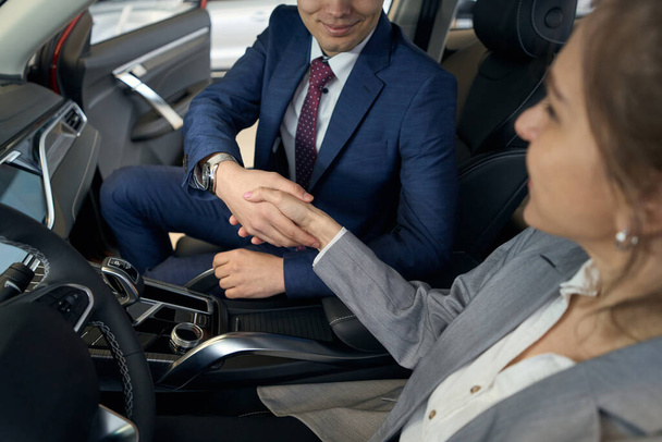 Businessman and lady in suit shaking hands while sitting on front seats in automobile - Photo, Image
