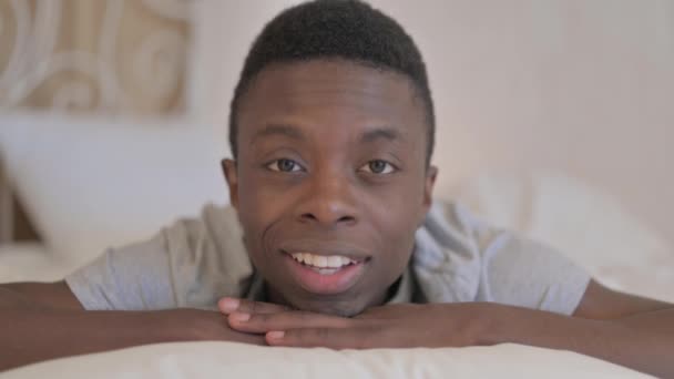 Parlare giovane africano fare video chat mentre sdraiato su stomaco a letto - Filmati, video