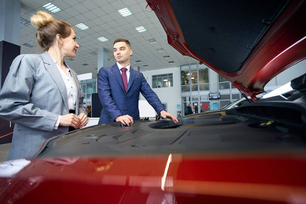 Smiling man and lady in suits standing near the hood of the car - Foto, Bild