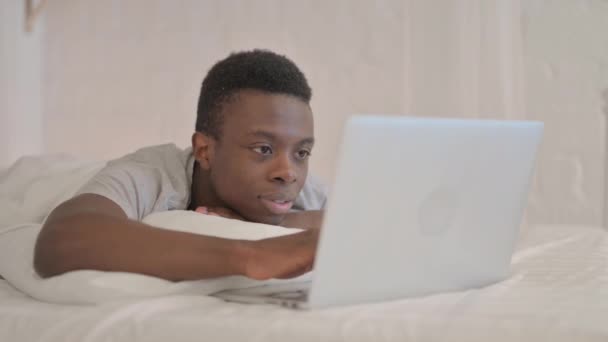 Genç Afrikalı Adam Laptop 'ta başarıyı kutlarken yatakta karın üstü yatıyor. - Video, Çekim