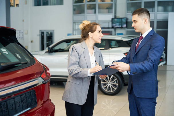 Счастливая деловая леди и мужчина в костюме заключают сделку в автосалоне - Фото, изображение