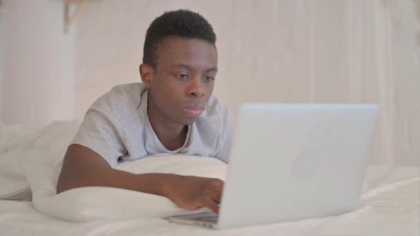 若いアフリカ人男性がカメラで笑顔でベッドに横たわっています - 映像、動画