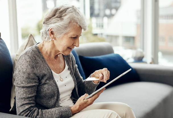 Покупаю подарки для внуков. пожилая женщина держит свою кредитную карту во время просмотра цифрового планшета - Фото, изображение
