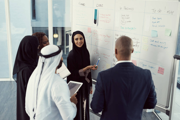 Sie leitet ihr Team mit einem Lächeln. Aufnahme einer Gruppe unterschiedlicher Geschäftskollegen, die gemeinsam an einem Whiteboard in ihrem Büro arbeiten - Foto, Bild