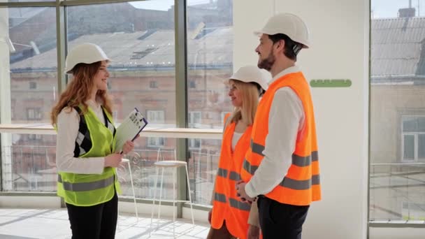 Female and male investors, wearing protective helmets, gather to meet with a real estate agent or broker to discuss the purchase or sale of a property. Office for new business, cafe or restaurant - Footage, Video