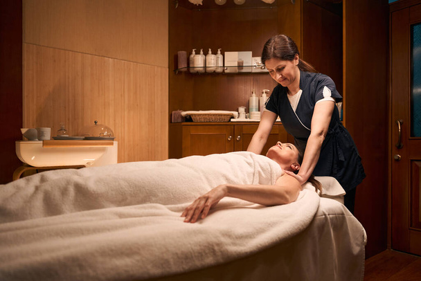 Fisioterapeuta enfocado presionando sobre los hombros del cliente del spa sonriente durante la sesión de masaje - Foto, imagen