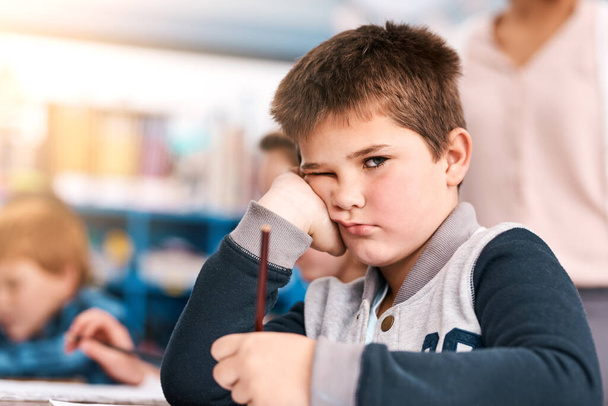 This little guy needs some motivation. Portrait of shot of a grumpy elementary school kid sitting in class trying to do school work - Zdjęcie, obraz