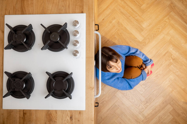Femme seule assise sur un plancher de cuisine, vue d'en haut avec surface de cuisson devant. Concept de nouvel équipement de cuisine - Photo, image