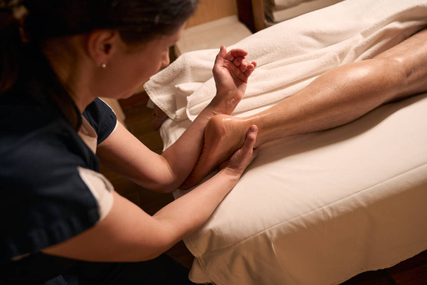 Photo recadrée d'un thérapeute spa massant le pied d'un homme adulte à l'aide d'un avant-bras - Photo, image