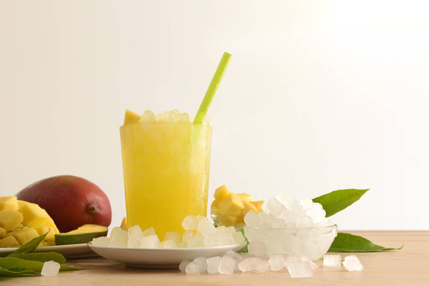 Detail of mango drink with a lot of ice on a wooden kitchen bench with fruit and a bowl with ice around it isolated background. Front view. Horizontal composition. - Φωτογραφία, εικόνα