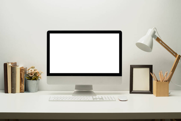 Falsificare computer schermo vuoto con tastiera, lampada, cornice e libri sul tavolo bianco. - Foto, immagini