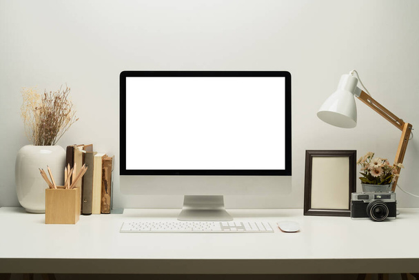 Vue de face de l'ordinateur à écran blanc avec clavier, lampe, cadre photo et livres sur table blanche. - Photo, image