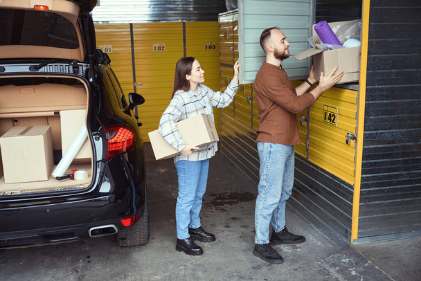 Un par de personas contentas de pie detrás del coche y apilando cajas de cosas en el casillero - Foto, Imagen