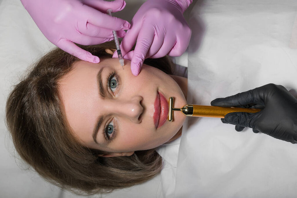 Injection process under facial skin at eye area with syringe. Young happy woman lying during procedure. Beautician does it carefully. High quality photo - Foto, afbeelding