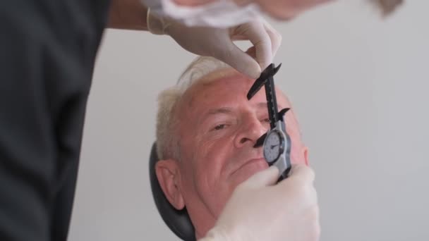 Портрет доктора-хирурга, оставляющего отметины на мужском лице, пожилого человека. Высококачественное 4k видео - Кадры, видео