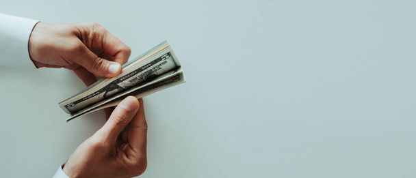 високий кут зору чоловіка в білій сорочці з довгим рукавом, що рахує доларові банкноти за білим столом, в панорамному форматі, який використовується як веб-банер
 - Фото, зображення