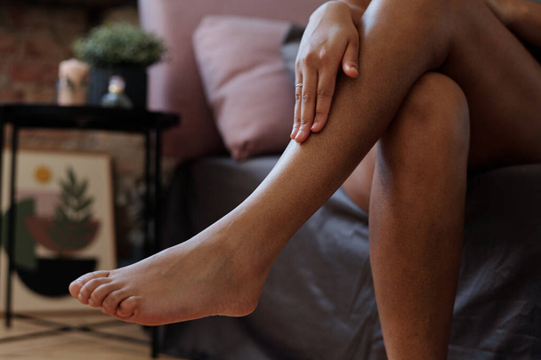 Close-up of legs of young woman touching her smooth skin after shaving and applying hydrating or nourishing cream in the morning - Foto, afbeelding
