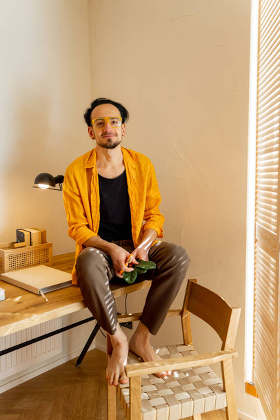 Portrait of creative man sitting on wooden table with books at workspace of stylish apartment. Hobby, creativity and home office concept - Foto, afbeelding