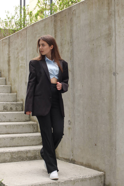 Portrait shooting of a stylish girl. Dark shades. Trends of spring and summer 2023. Business lady. Classic jacket and black pants. Blue shirt. Business center. Office work - Fotografie, Obrázek