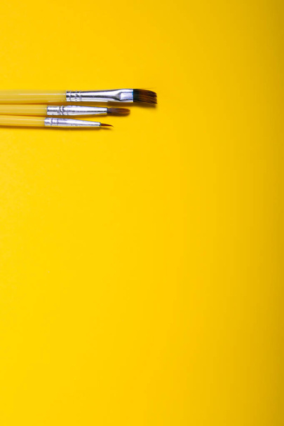 Un conjunto de pinceles de diferentes tamaños sobre un fondo amarillo. - Foto, imagen