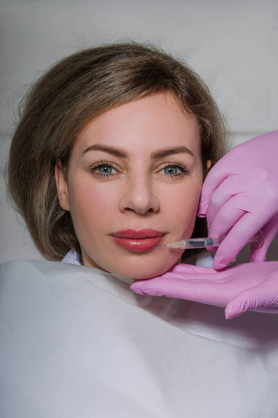 Young caucasian woman getting botox cosmetic injection in the lips. Beautiful woman gets botox injection in her face. Adult girl gets cosmetic injection of botox in a clinic. Beauty treatments. High - Foto, afbeelding