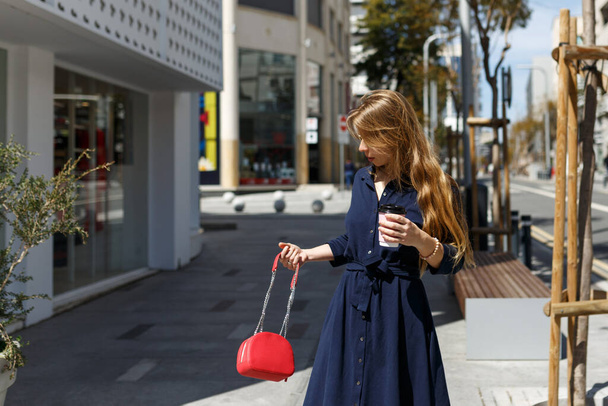 Снимок красивой молодой женщины в платье, переходящей улицу, держа в руках кофе и глядя в сторону. Цитрус, Никосия  - Фото, изображение
