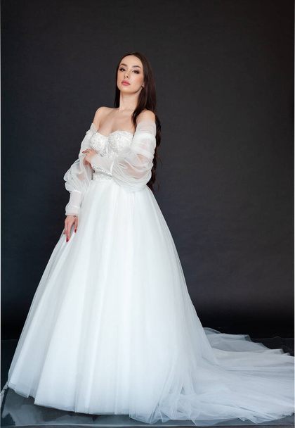 mooie bruid in een witte jurk op een zwarte achtergrond - Foto, afbeelding