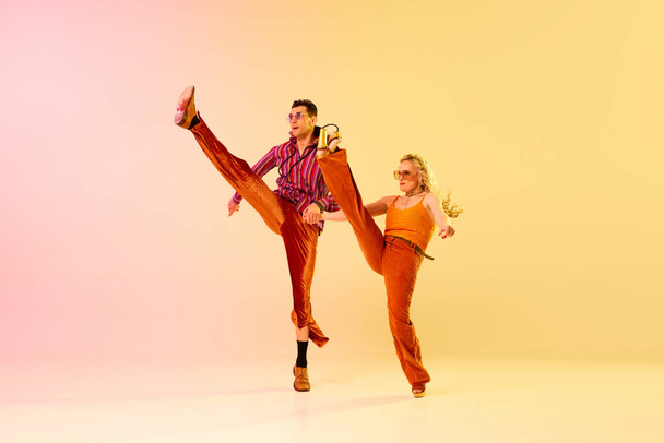 Disco dance. Active, expressive couple, man and woman in vintage clothes making performance against gradient pink yellow background. Concept of retro style, dance, fashion, art, hobby, music, 70s - Foto, Imagem
