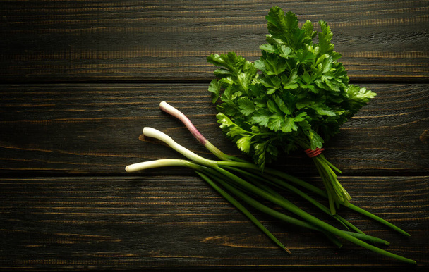 A bunch of green fresh fragrant parsley and green onions on a dark kitchen table before adding to food for taste and smell. Space for menu or recipe. - Foto, Imagem