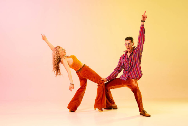Artistic, expressive couple, man and woman emotionally dancing disco dance against gradient pink yellow background. Performance. Concept of retro style, dance, fashion, art, hobby, music, 70s - Фото, изображение