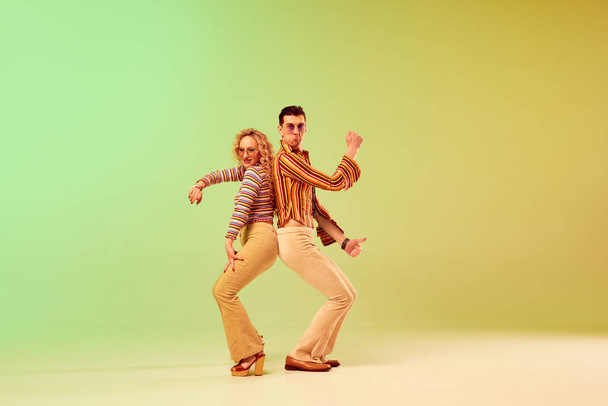 Choreography. Two talented people, autistic man and woman in vintage clothes dancing against gradient green yellow background. Concept of retro style, disco dance, fashion, art, hobby, music, 70s - Foto, Bild