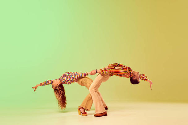 Jovem expressivo emocional e mulher bonita em roupas de estilo vintage dançando dança retro contra gradiente verde fundo amarelo. Conceito de estilo retro, dança, moda, arte, hobby, música, anos 70 - Foto, Imagem