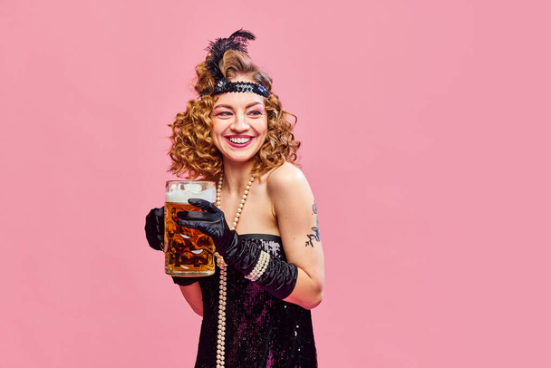 Gros plan portrait d'une femme souriante heureuse en robe de style rétro buvant de la bière fraîche avec plaisir sur fond rose. Concept de boissons, alcool, Oktoberfest, festivals, repos, vacances, annonce - Photo, image