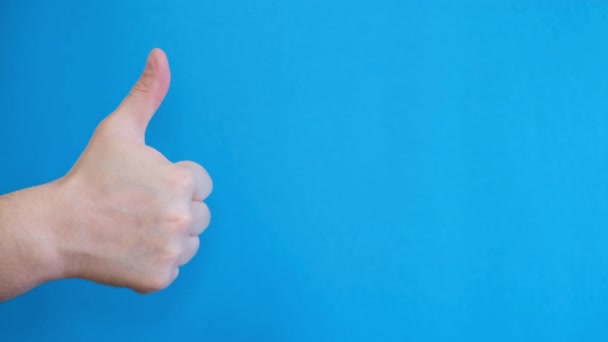 Egy kék hátterű kéz egy hüvelykujjat mutat. Férfi kéz bemutató osztály kék háttér. - Felvétel, videó