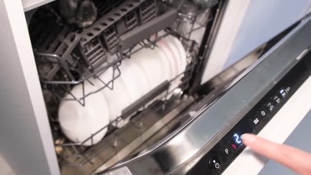 Una mano femenina presiona los botones de un lavavajillas automático para iniciar el programa. Cargando el lavavajillas - Imágenes, Vídeo