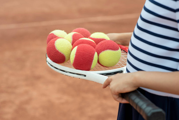 Kids player tennis. Racquet and legs and ball. Summer activities for children in the tennis club. Cropped image of sports little girl on tennis court. Athletic child girl hits tennis ball with a racke - Photo, Image