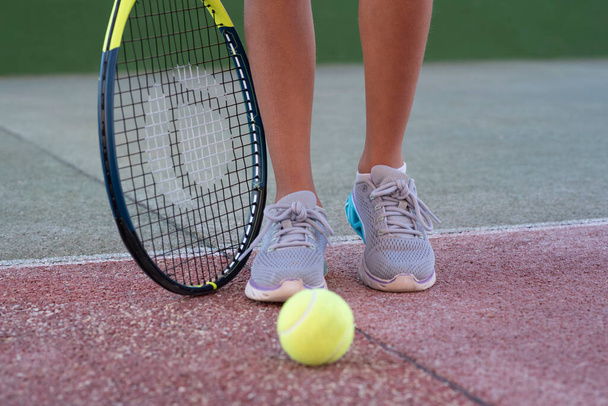 子供テニス選手。ラケットと足とボール。テニスクラブで子供のための夏の活動。テニスコートにいるスポーツ少女のトリミングされたイメージ。アスレチック子供の女の子ヒットテニスボールとともにAラック - 写真・画像