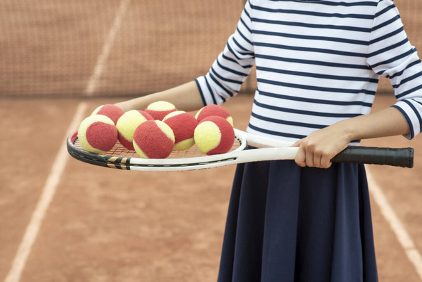 Παιδικό τένις. Ρακέ, πόδια και μπάλα. Καλοκαιρινές δραστηριότητες για παιδιά στο τένις κλαμπ. Καλλιεργημένη εικόνα ενός μικρού αθλητικού κοριτσιού στο γήπεδο του τένις. Αθλητικό κορίτσι παιδί χτυπά μπάλα του τένις με ένα racke - Φωτογραφία, εικόνα