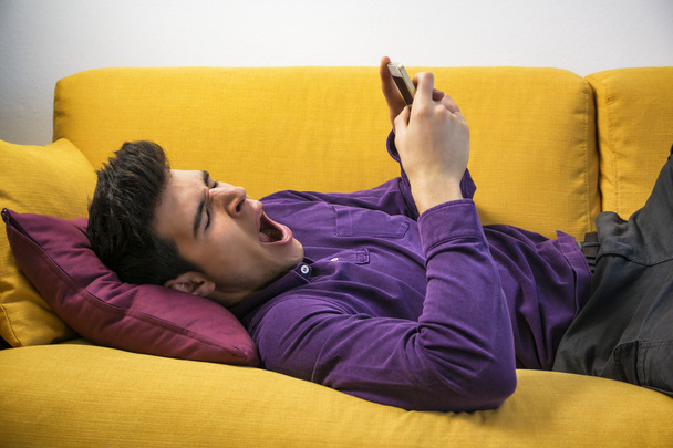 Man using cell phone and yawning, tired - Foto, afbeelding