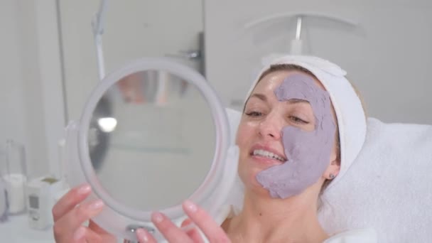 Fiatal nő lila csillogó csillogó maszkkal az arcán a spa szalonban. A bőrápolás fogalma. - Felvétel, videó