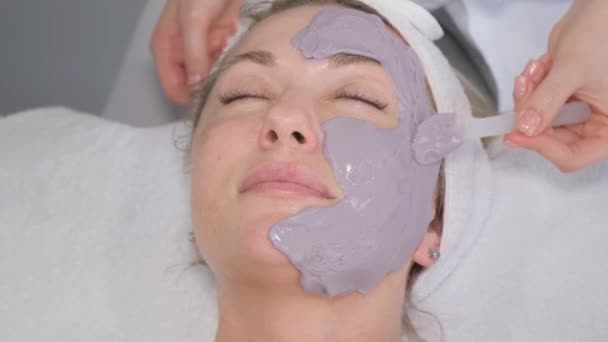 Cosmetisch schoonheidsmasker voor gezicht in schoonheidssalon. Spa procedures, ontspanning en huidverzorging. Een vrouw ontvangt gezichtsverzorging van een cosmetoloog in een spa salon. - Video