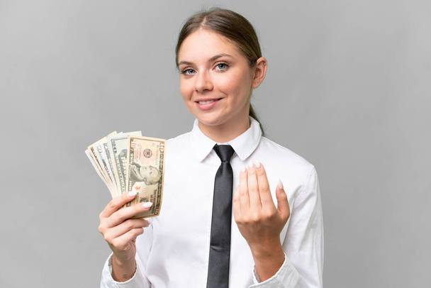Mladá obchodnice běloška drží peníze nad izolovaným pozadím a zvou ji, aby přišla s rukou. Jsem rád, že jsi přišel. - Fotografie, Obrázek