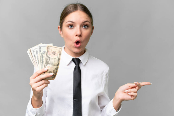 Young business caucasian woman holding money over isolated background surprised and pointing side - Фото, зображення