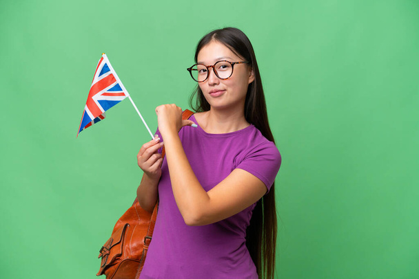 Young Asian woman holding an United Kingdom flag over isolated background proud and self-satisfied - 写真・画像