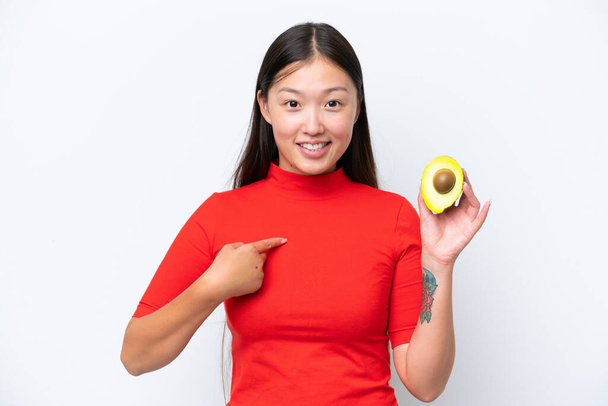 Young Asian woman holding an avocado isolated on white background with surprise facial expression - Фото, изображение