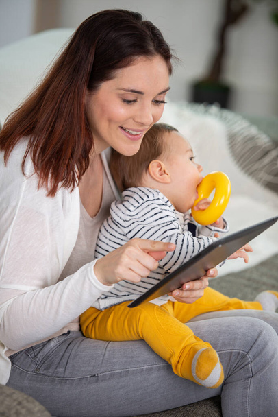 Mãe com bebê usando tablet digital em casa
 - Foto, Imagem