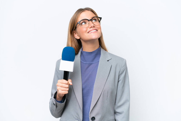 Joven presentadora de televisión mujer caucásica aislada sobre fondo blanco mirando hacia arriba mientras sonríe - Foto, Imagen