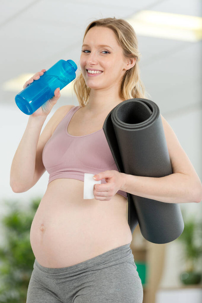 pregnant woman holding exercise mat and bottle of water - Foto, afbeelding