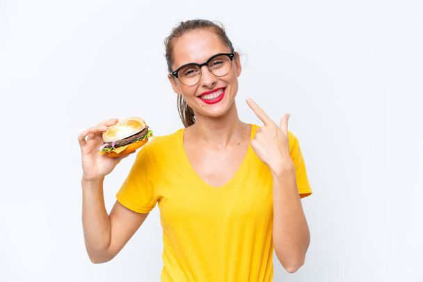 Young caucasian woman holding a burger isolated on white background giving a thumbs up gesture - Foto, imagen